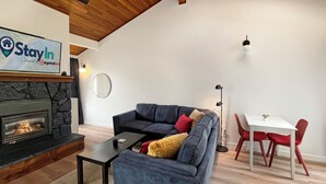 A modern living room with a stone fireplace, a blue sofa, a small table, and a dining area with red chairs.