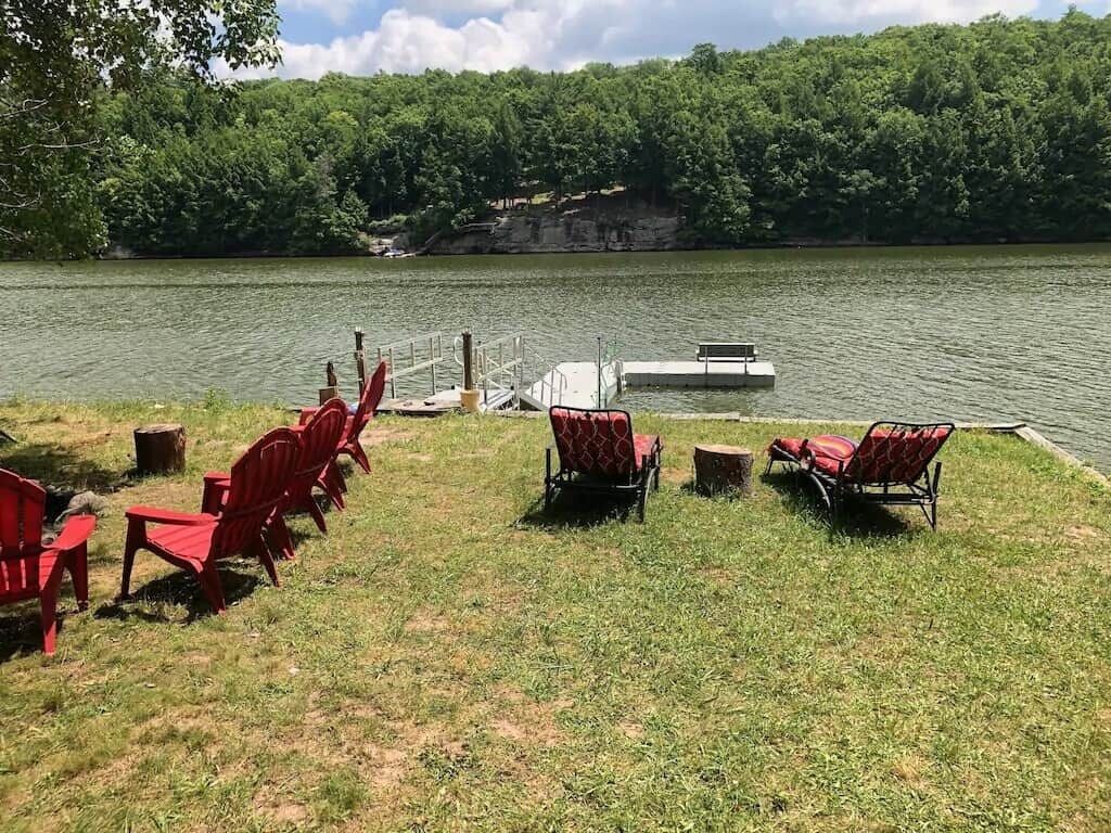 Un cadre idyllique au bord du lac, avec des chaises Adirondack rouges, une jetée et une pelouse.