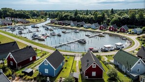 Ein Yachthafen mit vertäuten Booten, eine kleine Anlegestelle und Häuser mit roten und blauen Fassaden.