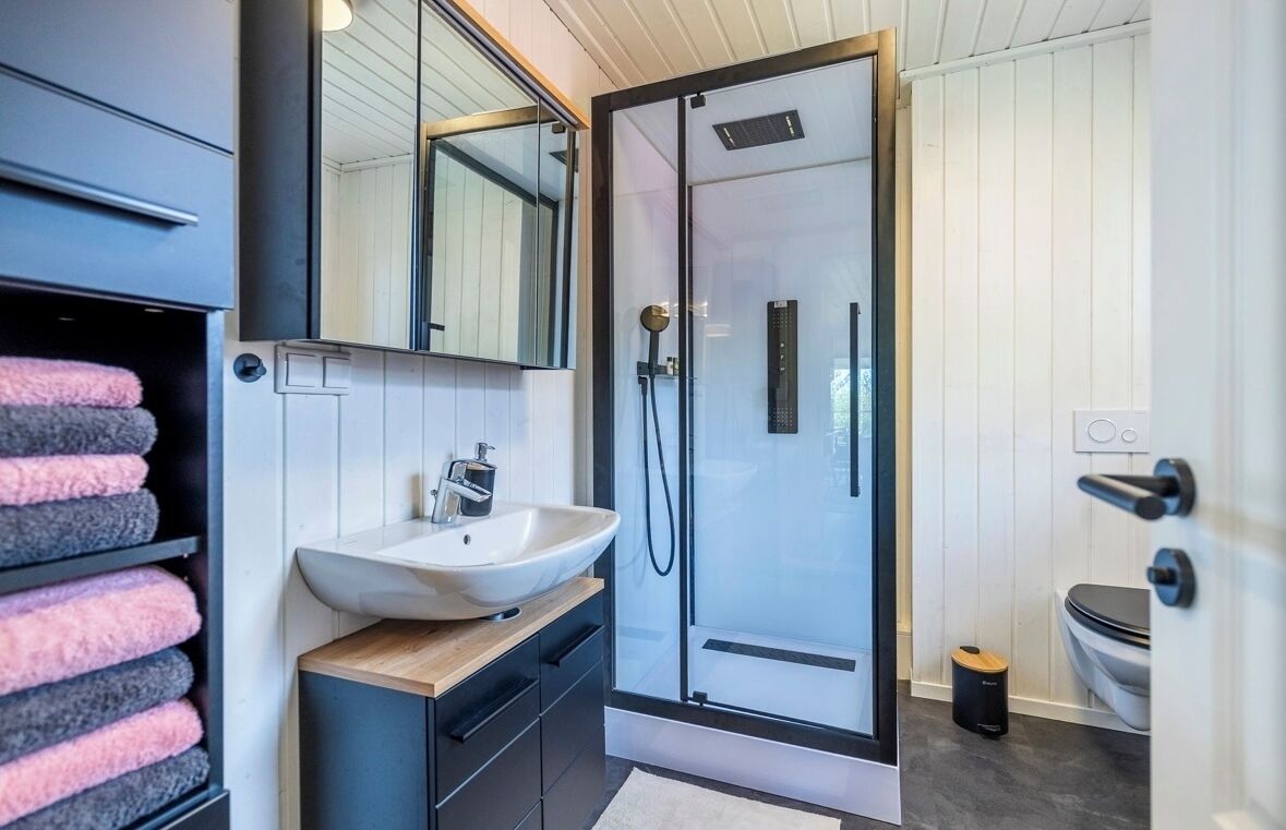 Een moderne badkamer met een douchecabine van glas, een witte wastafel en een houten badkamerkast.