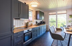 A modern kitchen with grey cabinets, a wooden countertop, and a built-in oven. There is a dining area with a table and chairs, and large windows providing natural light. - Quiet time out in the Rotkehlchen vacation home (Wandlitz)