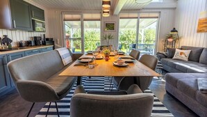 Eine moderne Küche mit integrierten Geräten, ein Essbereich mit Holztisch und -stühlen sowie eine gemütliche Sitzecke mit Sofa und Sesseln.