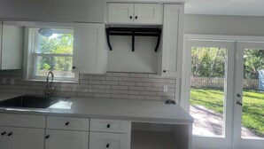 A kitchen with white cabinets, a countertop, a window, and a door leading to a backyard. - Beautiful 2-bedroom house with AC in peaceful Palm Valley (Palm Valley)