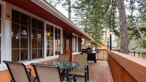 A covered patio with a table and chairs, a grill, and a view of trees. - Martindale Manor | Historic Mountain Retreat w/ Hot Tub & Game Room (Cascade-Chipita Park)