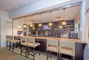 A bar area with a long counter, multiple bar stools, a television screen, and shelves with bottles. - Family Friendly 3bd Villa w/Pvt Pool Nxt to Disney (Kissimmee)
