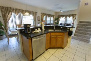 A kitchen with a dishwasher, a sink, and a countertop. There is a chair and a table in the adjacent dining area. - Spacious 4BR/3BA Encantada Townhome - Sleeps 8 Near Disney (Kissimmee)