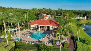 Una casa grande con piscina, rodeada de palmeras y un lago.