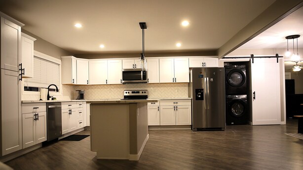 A modern kitchen with white cabinets, a central island, stainless steel appliances, and a built-in washer and dryer.