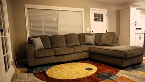 A living room with a sectional sofa, a patterned rug, and a door with a window.