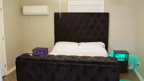 A bedroom with a bed, a ceiling fan, an air conditioner, and a nightstand.