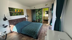 A bedroom with a bed, a nightstand, a lamp, a painting, and a view of a bathroom.