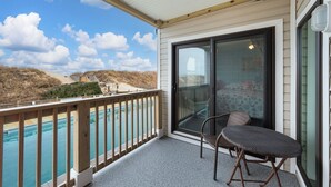 Un balcon avec vue sur une piscine et des collines, une porte-fenêtre coulissante et deux fauteuils en osier.