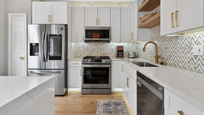 A modern kitchen with white cabinets, stainless steel appliances, a microwave, a coffee maker, and a sink with a gold faucet.