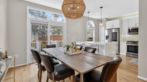 A modern kitchen with white cabinets, stainless steel appliances, and a dining area with a wooden table and leather chairs.