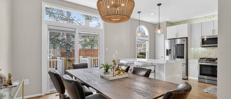 A modern kitchen with white cabinets, stainless steel appliances, and a dining area with a wooden table and leather chairs.