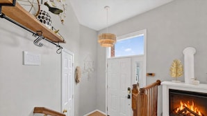 A hallway with a fireplace, a wooden staircase, and a door leading to another room.