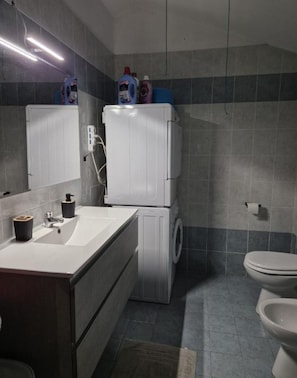A bathroom with a sink, mirror, toilet, and stacked washer-dryer unit. - Margaret House (Tribiano)