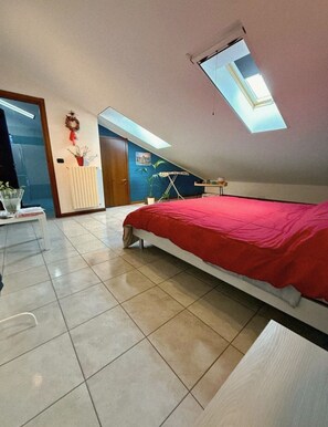 Ein Schlafzimmer mit Bett, Schreibtisch, Heizkörper, Fenster und Tür.