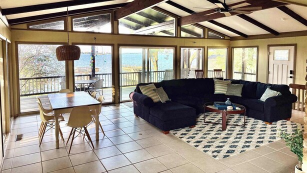 A spacious living area with a large dark-colored sofa, a dining table with chairs, and a view of the outdoors through large windows. - Lakeview Lookout - Stunning Views! (Tool)