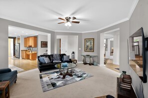 A spacious living room with a black leather sofa, a glass coffee table, and a ceiling fan.