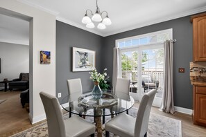A dining area with a glass table, chairs, a vase with flowers, and a painting on the wall.