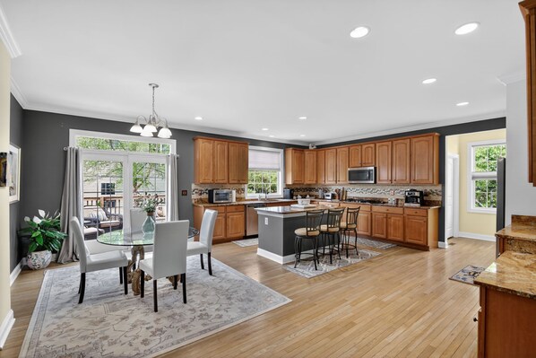 A modern kitchen with wooden cabinets, a central island, and a dining area with a glass table and chairs.