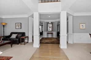 A spacious living room with a black leather sofa, a wooden coffee table, and a floor lamp. A hallway leads to a dining area with a wooden table and chairs. - Spacious Fredericksburg Home in Quiet Cul-de-Sac (Fredericksburg)