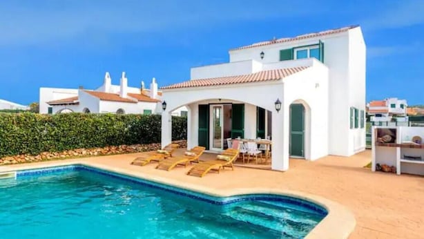 Una villa moderna con piscina, sillas de descanso y un patio cubierto.