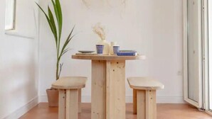 Una mesa de madera con dos taburetes, un florero y una planta en maceta en una habitación con suelo de baldosas y un ventanal.