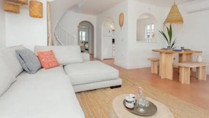 Una sala de estar moderna con un sofá blanco, un comedor con muebles de madera y una escalera que sube a otro nivel.
