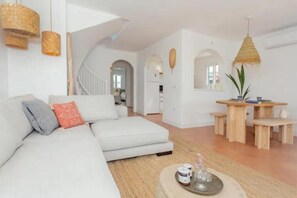 Ein modernes Wohnzimmer mit einem weißen Sofa, einem Essbereich mit Holzmöbeln und einer Treppe zu einer weiteren Ebene.
