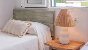 Una cama con cabecera de madera, una lámpara de noche y una ventana con vistas a follaje.