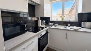 Una cocina moderna con armarios blancos, una estufa negra y un ventanal con vistas a un edificio de ladrillo.
