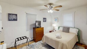 A bedroom with a bed, a dresser, a ceiling fan, and artwork on the walls. - The Three Seasons | Centrally located house in Lak (Lake Leelanau)
