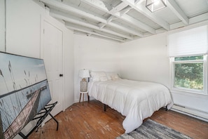 Un dormitorio con cama, un cuadro en la pared, una ventana con vistas y una puerta.