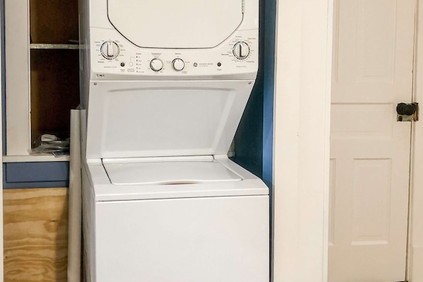 Una lavadora de carga frontal en un cuarto de lavado con piso de madera y una puerta blanca.