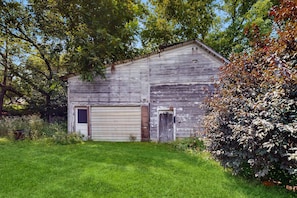 A rustic wooden barn with a garage, surrounded by lush greenery and trees.