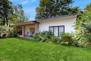 A single-story house with a covered porch, a small patio, and a well-maintained garden. - The Three Seasons | Centrally located house in Lak (Lake Leelanau)