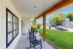 A covered porch with a bench, a lawn, and a view of a residential street.