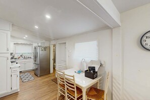 A compact kitchen with white cabinets, a refrigerator, and a dining area with a table and chairs. - The Three Seasons | Centrally located house in Lak (Lake Leelanau)