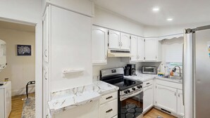 A modern kitchen with white cabinets, a black stove, a built-in oven, and a stainless steel refrigerator.