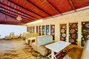 A restaurant with wooden flooring, cushioned seating, and a red ceiling. - Collection O Puthali Park (Mysore)