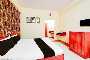 A hotel room with a bed, a red wardrobe, a small table with a kettle, and framed artwork on the wall. - Collection O Puthali Park (Mysore)