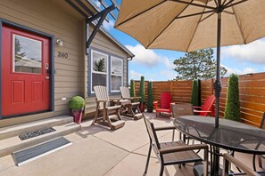 Ein Haus mit roter Tür, Hausnummer 240, einer Veranda mit Holzstühlen, einem Tisch und einem großen Sonnenschirm.