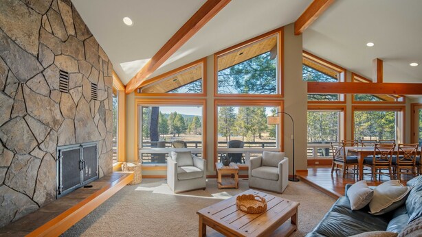 Amplia sala de estar con chimenea de piedra, ventanas grandes y un techo alto con vigas de madera.