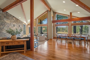 A spacious room with a stone wall, wooden beams, large windows, and a dining area. - Spacious 4bd/4bath Riverfront Retreat in Sunriver (Sunriver)
