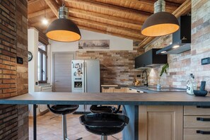 A kitchen with a brick wall, wooden ceiling, two pendant lights, a refrigerator, and a sink. - "Sunrise over the sea and relaxation on Etna: Green oasis near the pearls of Sicily. (Sicilia)