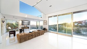 A modern living room with a large sofa, a fireplace, and a city view through floor-to-ceiling windows.