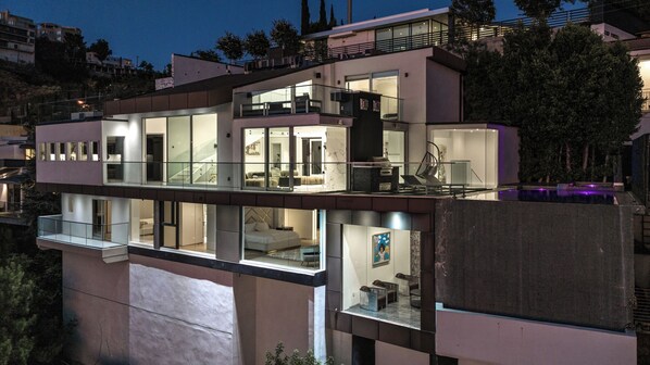 A multi-story modern house with large glass windows, a balcony, and a pool area.