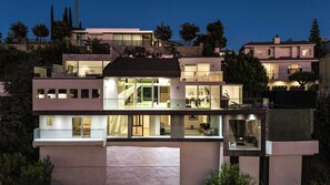 A multi-story modern house with large windows, a visible staircase, and a balcony.